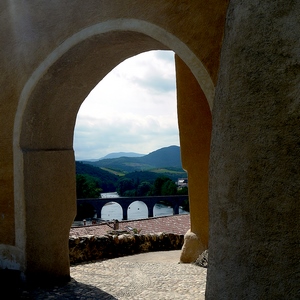 Arche s'ouvrant dans un mur cimenté sur un paysage de montagnes, rivière et pont. - France  - collection de photos clin d'oeil, catégorie rues